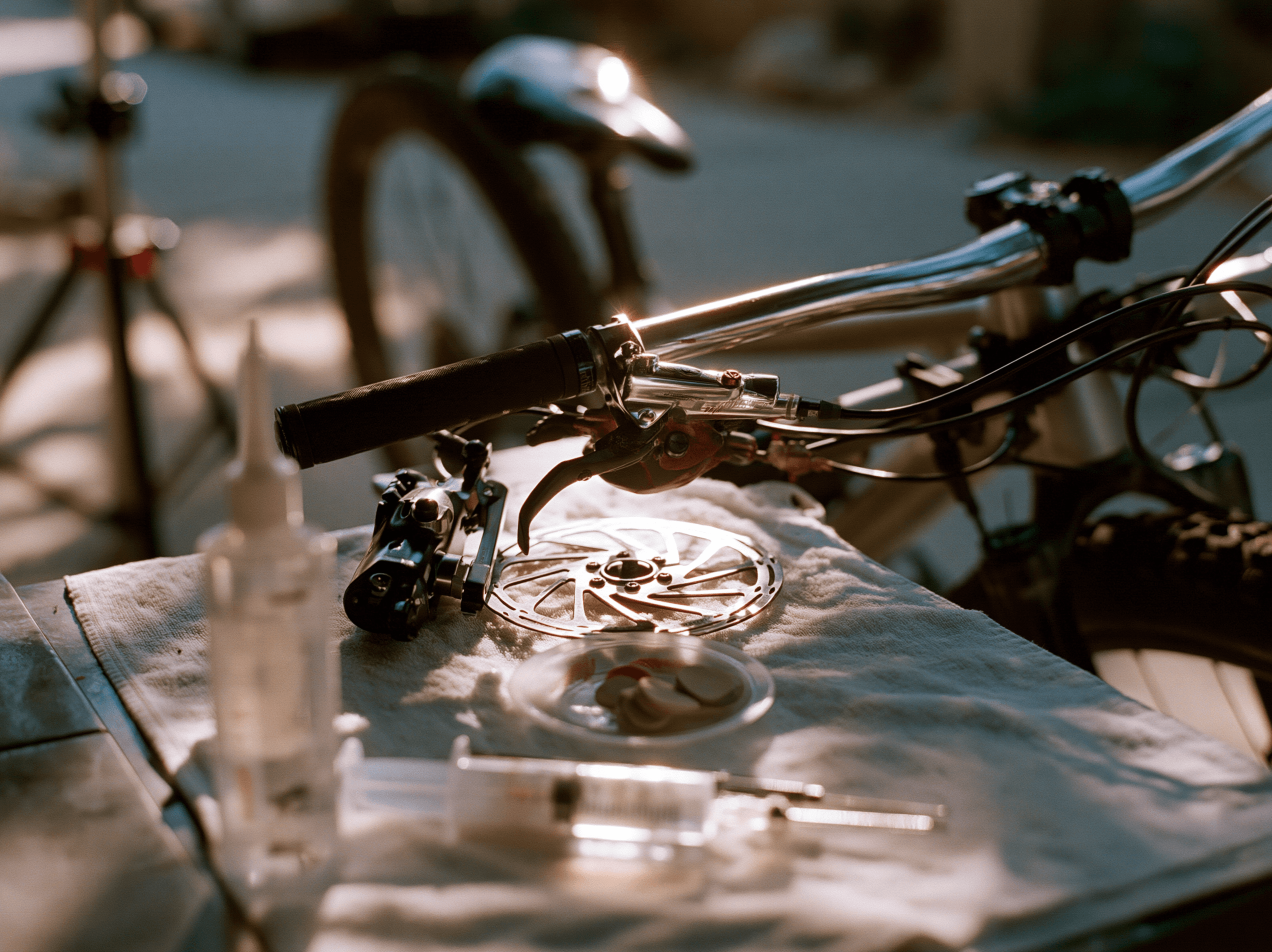 A hydraulic brake caliper, lever, and rotor on a white shop cloth with a syringe and bottle of brake fluid laid out for a bleed.