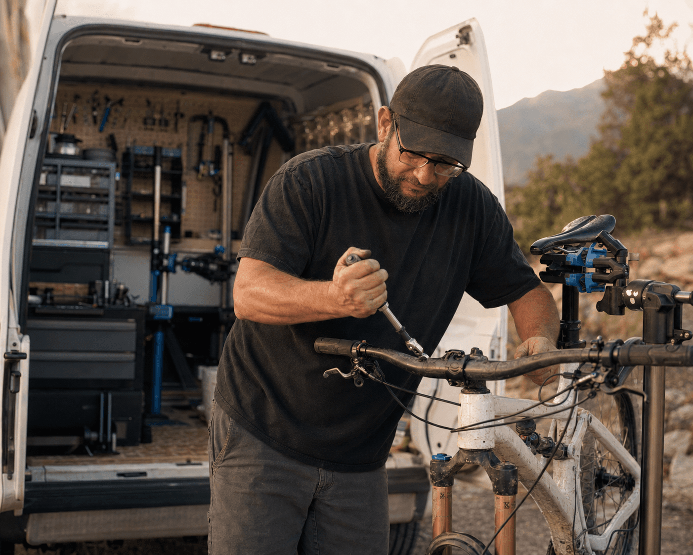 Seth Parsons working on a mountain bike's handlebars with a hex tool, his service van's open back doors and tool pegboard behind him.